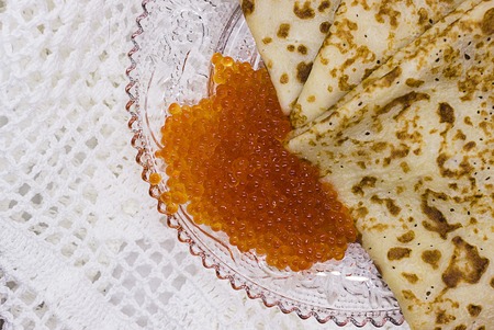 Traditional Russian pancakes with red caviar on a glass plate