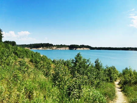 Beautiful blue lake surrounded by forest. Grass and flowers by the lake in a sandy quarryの写真素材