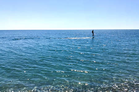 Silhouette of a man who is surfing on hydrofoils against the backdrop of the sea on a bright sunny...