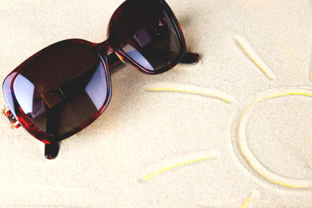 Brown sunglasses lie on the sand where the sun is drawn. summer and vacation concept