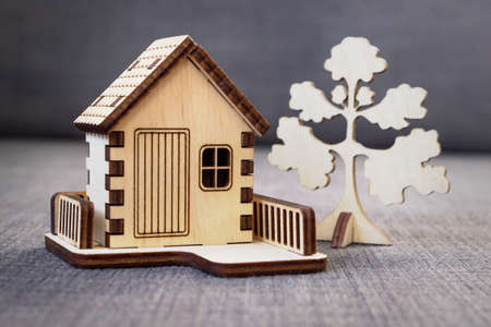 Wooden decorative toy house with a fence and a tree standing on a gray background. Buying or renting...