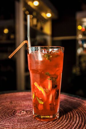 Red cocktail in a tall grain glass with fine ice and lemon, lime, mint leaves, berry, currants, cranberries and yellow straw. Drink in a glass for the menu restaurant, bar, cafe.の写真素材