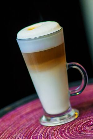 Delicious layered cappuccino or latte macchiato coffee served in a long glass. Cup of coffee in clear long glass on a tray.の写真素材
