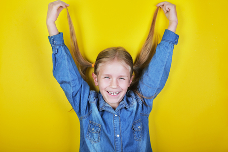 Laughing funny little girl standing on yellow background and holding ponytailsの写真素材