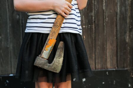 Smiling blond girl holding an axe in hands on wooden background. Halloween celebration,  horror...