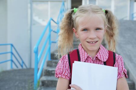 Back to school. Beautiful blond schoolgirl with red backpack and books outside the primary school , education conceptの写真素材