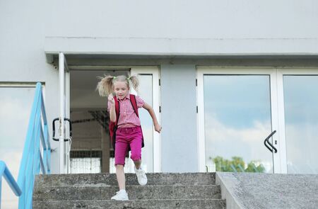 Back to school. Beautiful blond schoolgirl with red backpack running outside the primary school