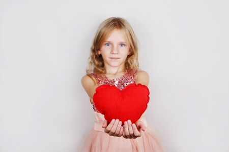 little beautiful blond girl with red heart on a white background. Child with a heart for Valentine's dayの写真素材