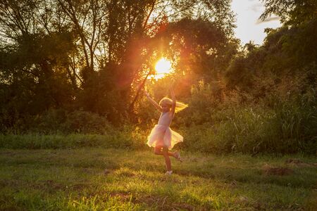 Happy little blonde girl in gray dress dancing in park, sunlight, sunsetの写真素材