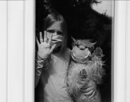 Sad girl wearing protection mask with dog looking out the window.Coronavirus covid-2019 ....
