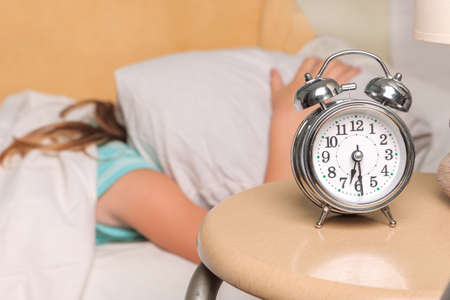 Little funny girl lying in bed and close ears while the alarm clock ring to wake her up in the...