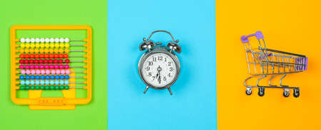 Back to school shopping concept. Abacus, alarm clock and shopping trolley on olorfull background,...