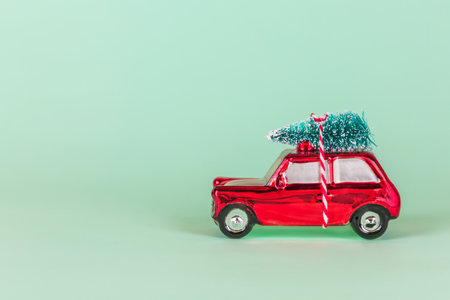 Red toy car with christmas tree decoration on turquoise background. Christmas, New Year holiday celebration conceptの写真素材