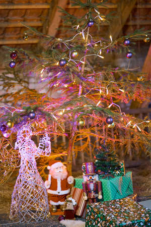 The center of a Christmas tree decorated with baubles and lights and an angle standing beneath it with some presents. Illuminated with red and purple colors for a special and warm feeling.の写真素材