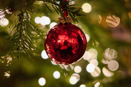 A red Christmas tree decoration with the photographer visible in the reflection. In the background the soft lights of the tree.の写真素材