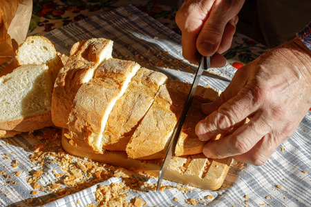 Male hands cutting wheaten bread on the wooden board, selective focusの写真素材
