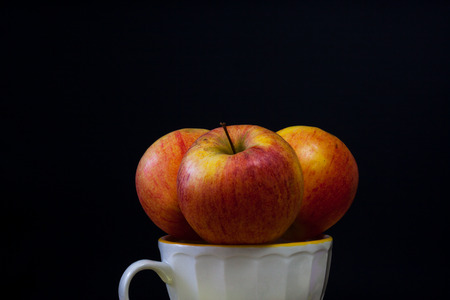 Three red apples in a cup of milk, fruit with black background and copy spaceの写真素材