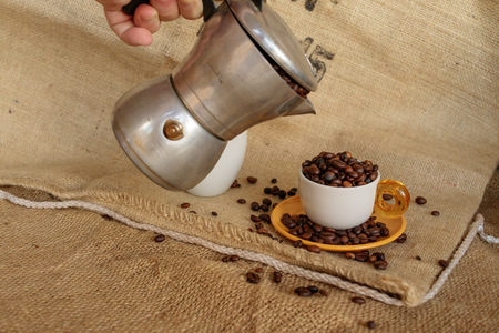 Tavigliano, Italy - August, 01, 2017: Hand of man with Italian moka pour coffee beans into the cup. Vintage still life style, jute bag in background.のeditorial素材