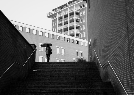 Dark Scenic city in the rain. Silhouette of person under the umbrella in urban environment.のeditorial素材