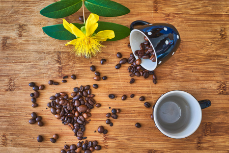 Two cups with coffee grains in shape of heart and yellow hypericum flower on wooden tableの写真素材