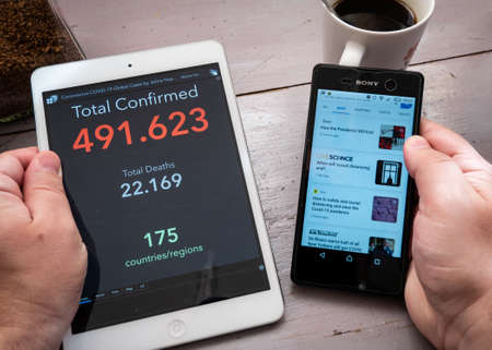 Man holds tablet in his hand with updated Coronavirus COVID-19 live statistic and in other hand smartphone with news on the table with coffee, Mexico, in March 26, 2020のeditorial素材