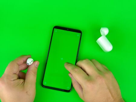 Man hands touch mobile phone with a vertical green screen and headphone, key smartphone technologyの写真素材
