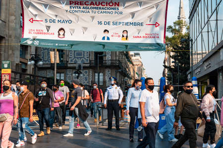 Crowd of ethnic people in masks walking past police officer with face shield under banner on street of Mexico City during coronavirus lockdown, Mexico, December 12, 2020のeditorial素材