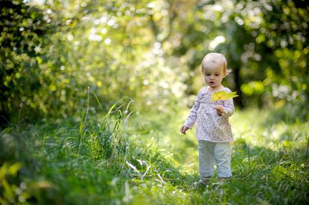 Little baby in a forest holding yellow leaf and looking at itの写真素材