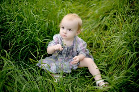 Little baby is sitting in a meadow in the grass holding flowerの写真素材