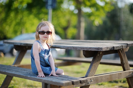 Adorable little girl sitting on a bench at summerの写真素材