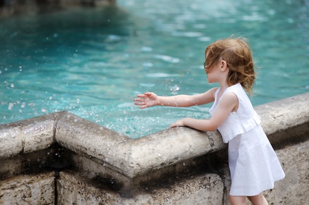 Funny little girl having fun by a city fountainの写真素材