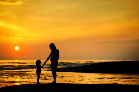 Pregnant mother and her child as silhouettes by the seaの写真素材