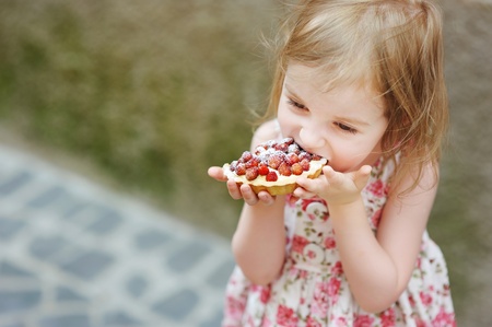 Little girl eating a strawberry tart outdoorsの写真素材