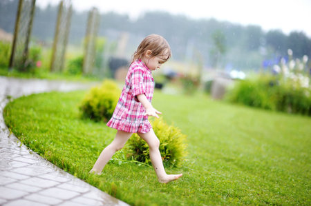 Little girl having fun under the rain in summerの写真素材