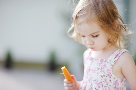 Adorable happy preschooler girl eating carrot outdoorsの写真素材