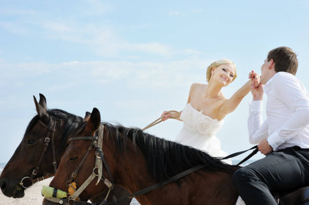 Beach wedding: bride and groom on a horses by the seaの写真素材