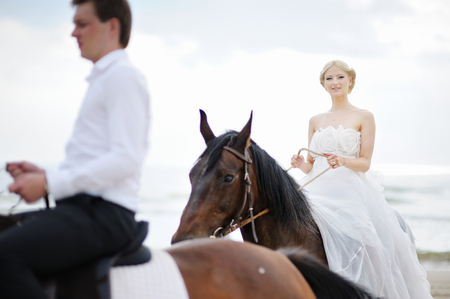 Beach wedding: bride and groom on a horses by the seaの写真素材
