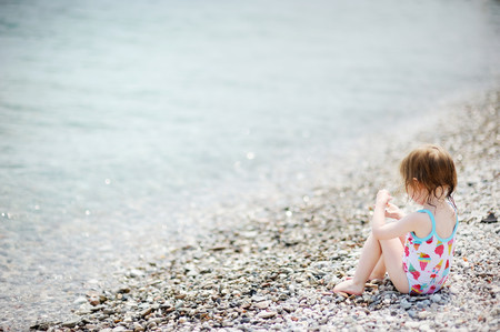 Cute toddler girl playing on pebble beachの写真素材