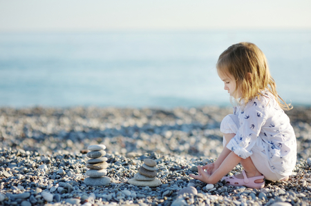 Cute little girl playing on pebble beachの写真素材