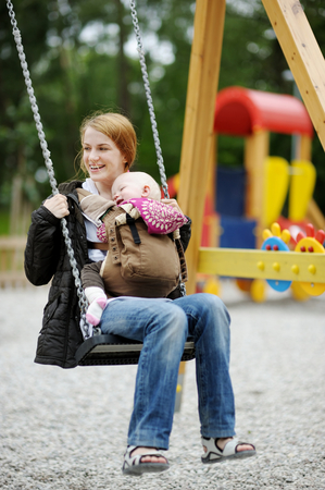 Young mother on a swing with baby in a babycarrierの写真素材