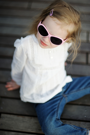 Adorable little girl in sunglasses sitting on a wooden floorの写真素材