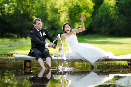 Bride and groom drinking champagne by the lakeの写真素材