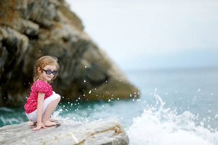 Adorable little girl sitting on a rock by a seaの写真素材