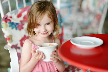 Adorable girl drinking hot chocolate in outdoor restaurantの写真素材