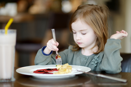 Cute little girl eating pancakes in a cafeの写真素材