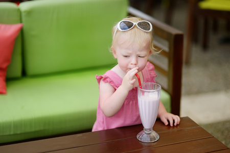 Adorable little girl drinking milkshake in outdoor restaurantの写真素材