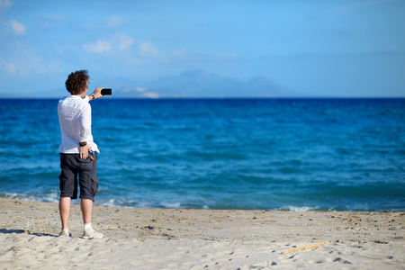 Man taking photo with mobile phone on the beachの写真素材