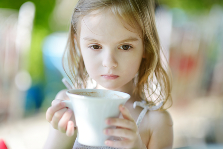 Adorable girl drinking hot chocolate in outdoor restaurantの写真素材