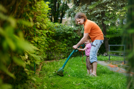 Father and a child cutting the grass with a lawn trimmerの写真素材