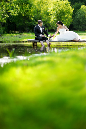 Bride and groom drinking champagne by the lakeの写真素材